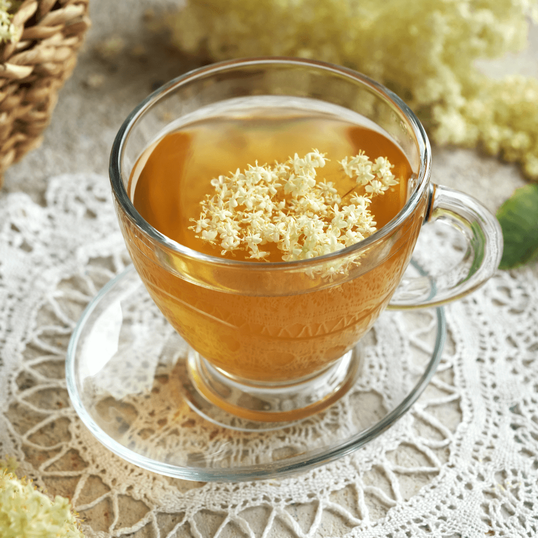 Naturopathe à Chavornay Une tasse de tisane aux fleurs de sureau posée sur une nappe en dentelle, symbolisant les pratiques de naturopathie et les soins naturels offerts par un naturopathe à Chavornay.
