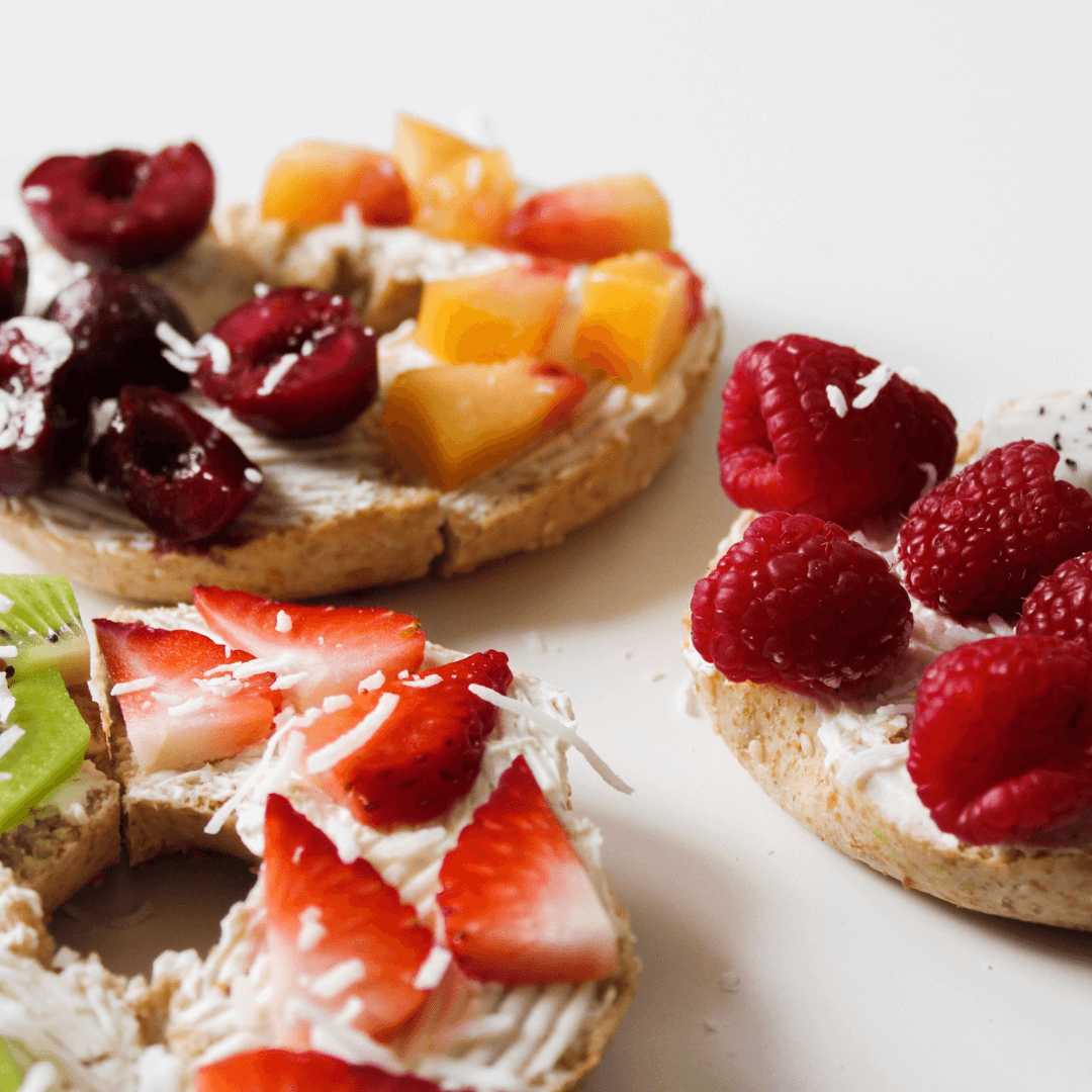 Conseils en nutrition à Orbe Des bagels garnis de fruits frais tels que des cerises, des pêches, des framboises, des fraises et du kiwi, illustrant les services de conseils en nutrition disponibles à Orbe.