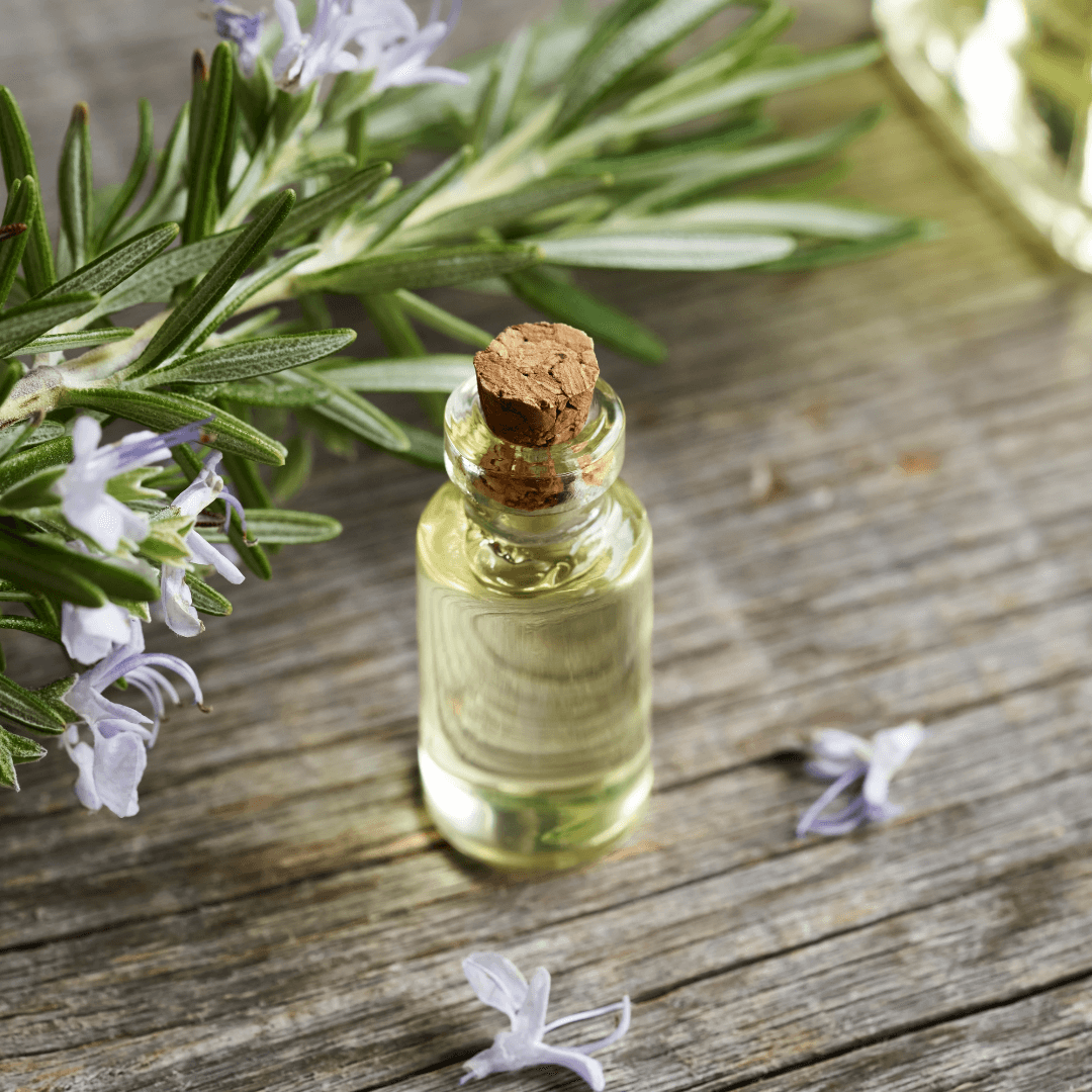 Naturopathe à Orbe Une petite bouteille d'huile essentielle avec un brin de romarin fleuri sur une table en bois, illustrant les pratiques et remèdes naturels utilisés par un naturopathe à Orbe.